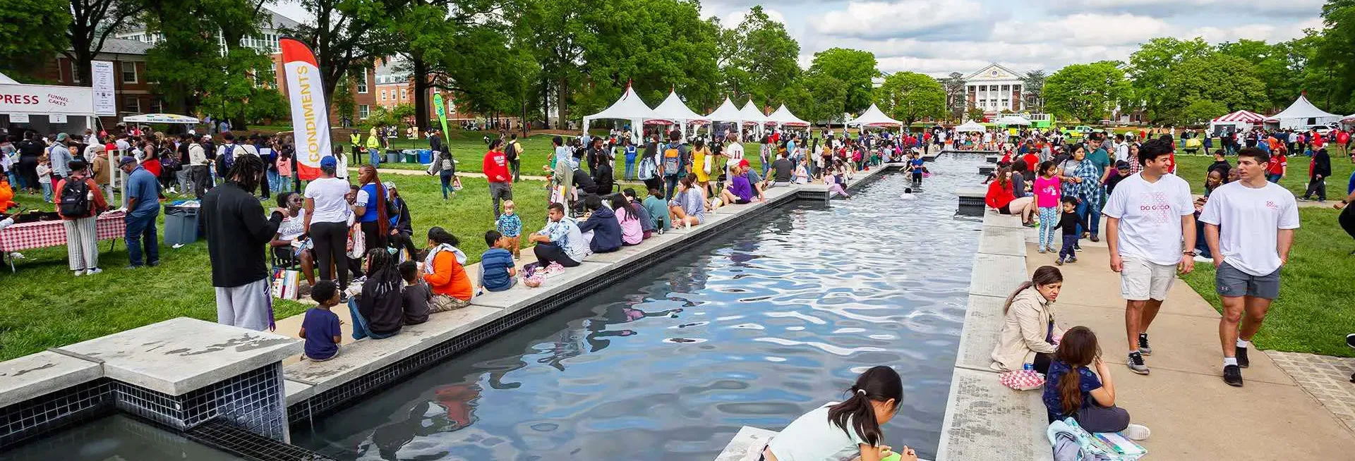 View of campus at the fountain on the mall, many people mill around, festive atmosphere with tents