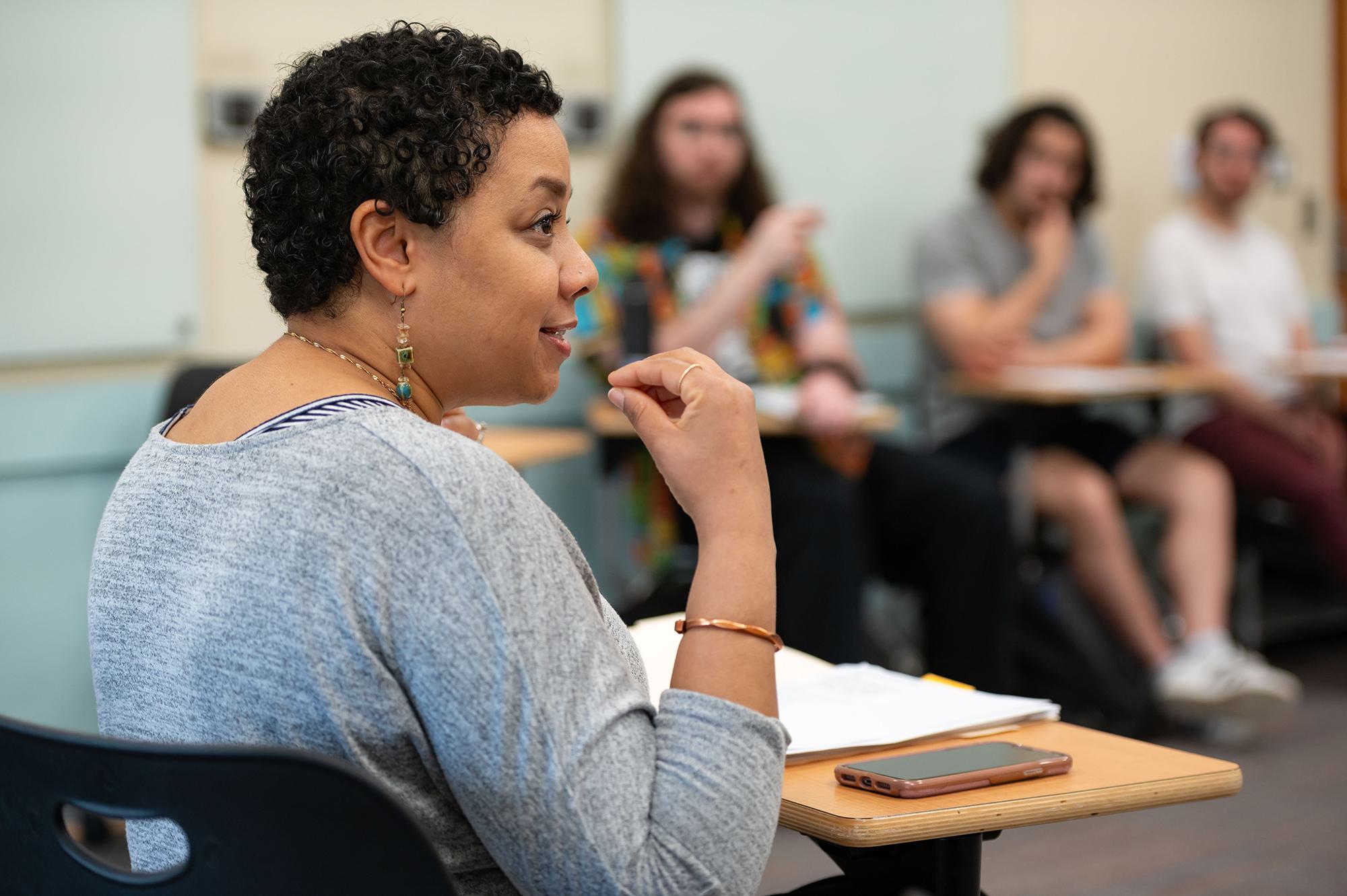 Professor sitting at a desk, speaking to class