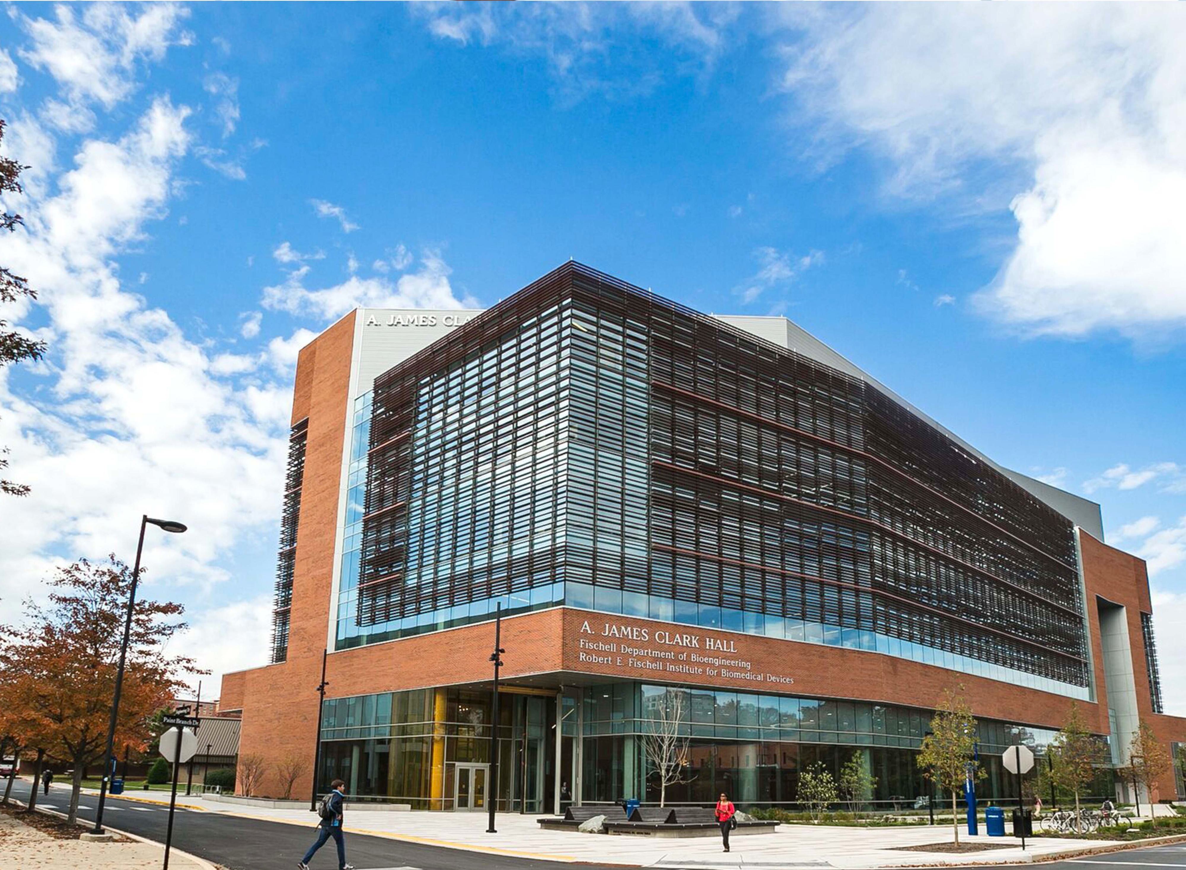 Exterior view of the James A. Clark School of Engineering building with students walking along the sidewalk underneath a blue sky.