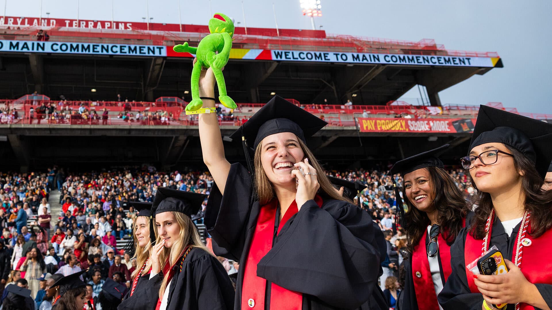 graduate holds up Kermit the Frog doll
