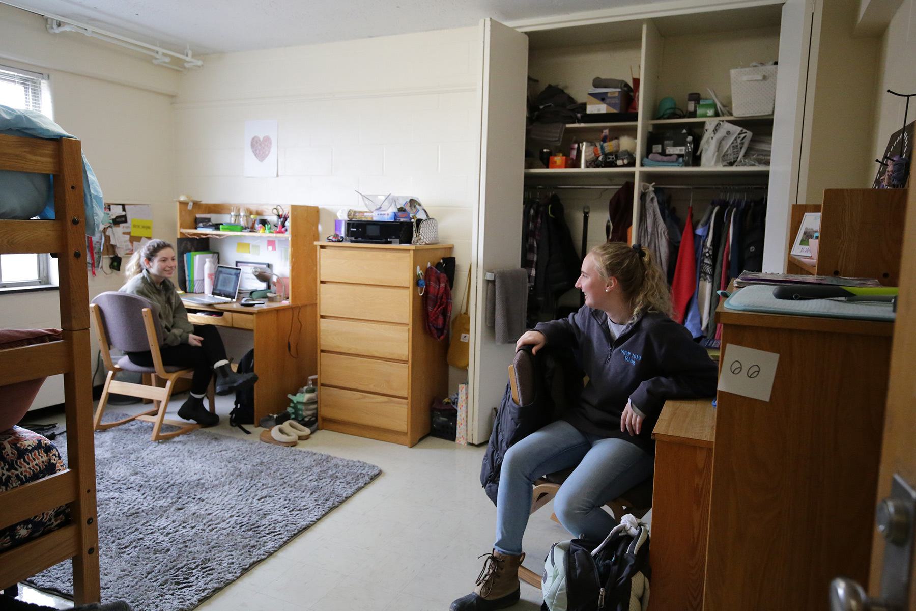 2 young woman sitting at their desks, talking in a dorm.
