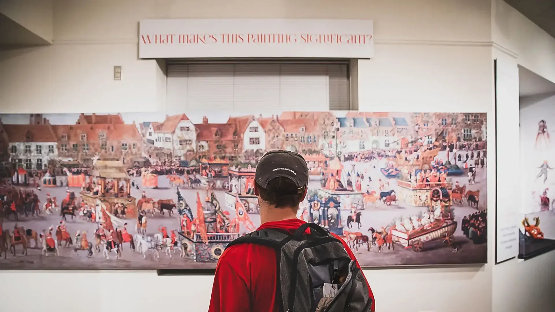 Person with backpack looking at a wide piece of art. Sign: What makes this painting significant?