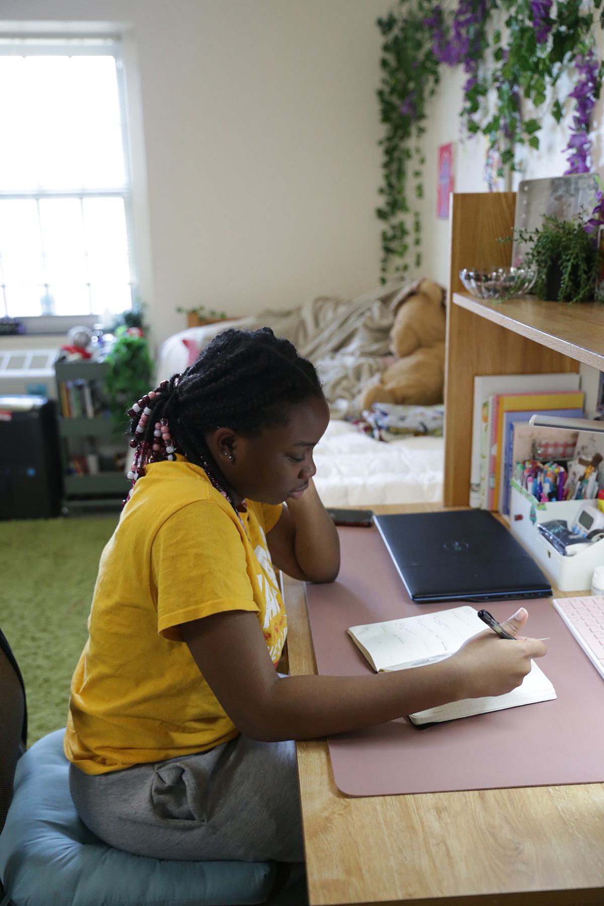 Young woman studying at a desk in a dorm room. Plants trail on walls