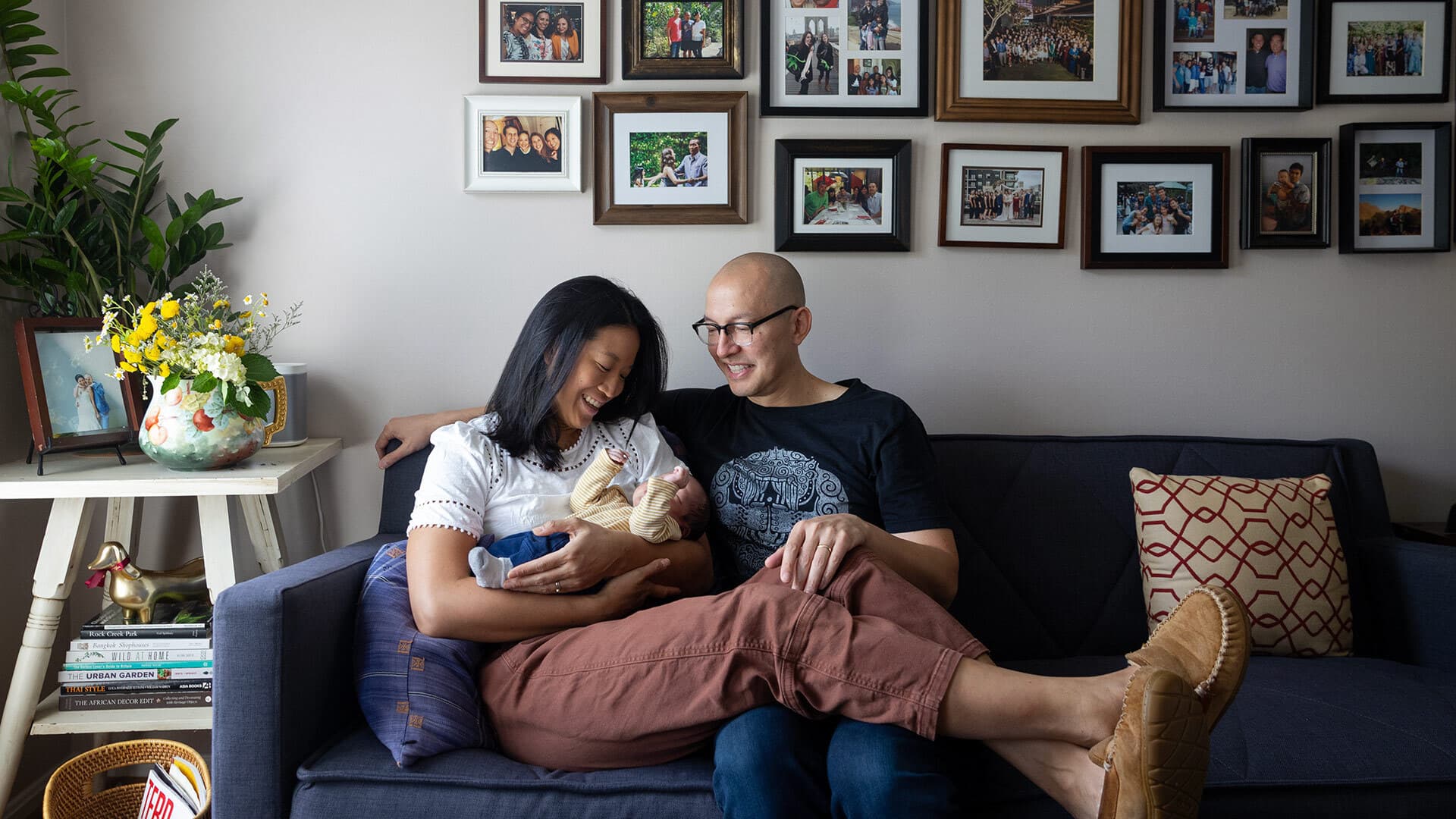 couple with baby on couch below picture frames on wall