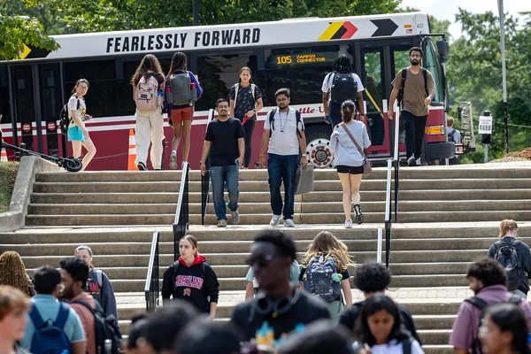 Students walking up and down steps. Bus in background with "Fearlessly Forward"