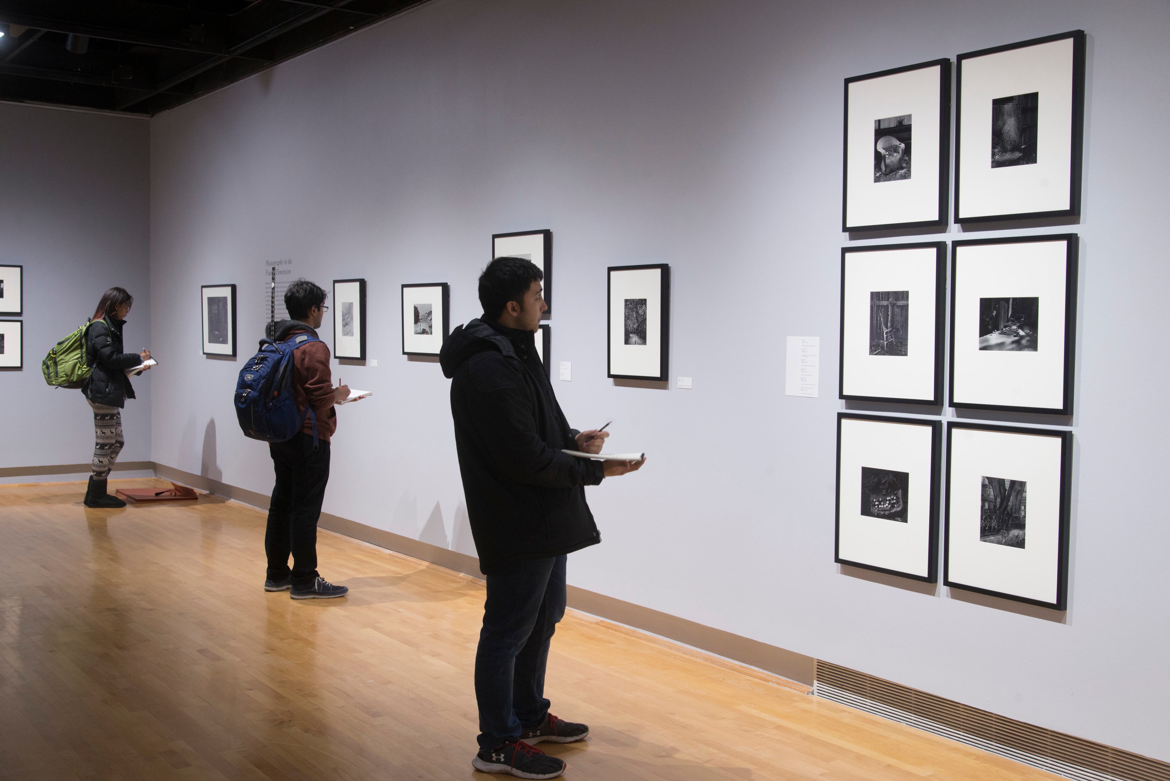 View of an art gallery, visitors looking at black and white framed photos on gray walls.