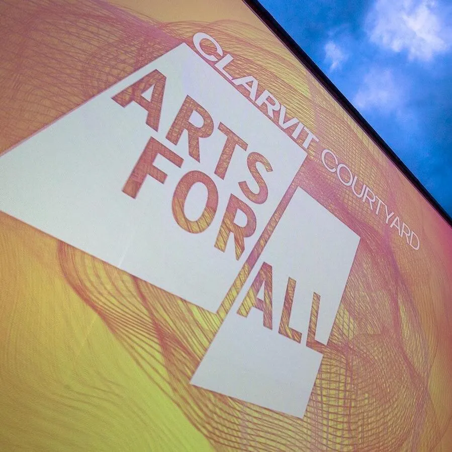 Sign at an angle: Clarvit Courtyard / Arts for All on yellow and pink sign. Background of a darkened sky