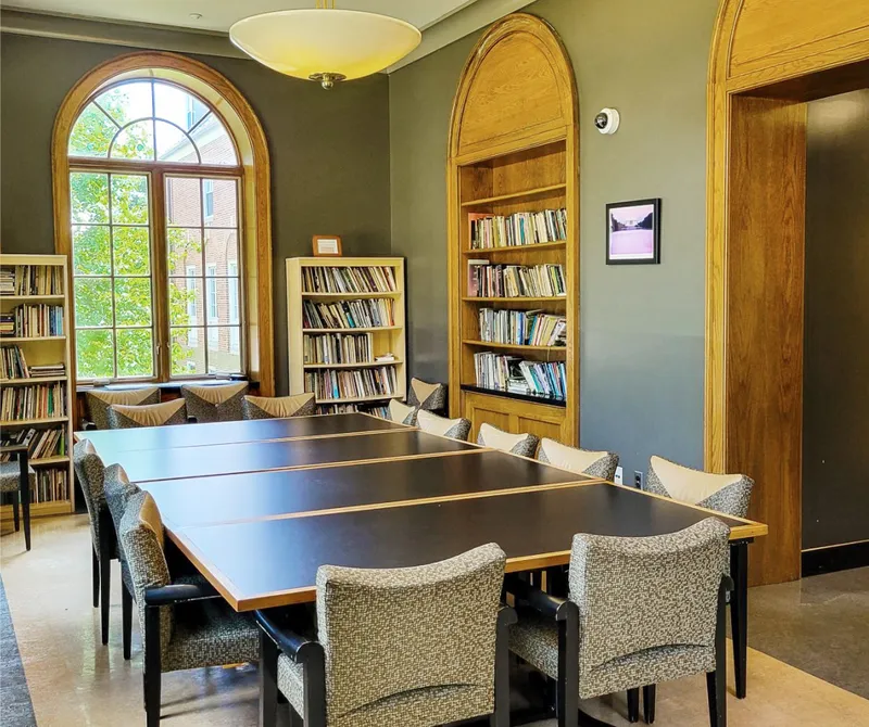 Room with large table with chairs around, book shelves on walls.