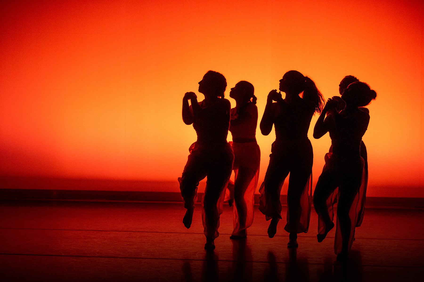 4 dancers backlit in orange
