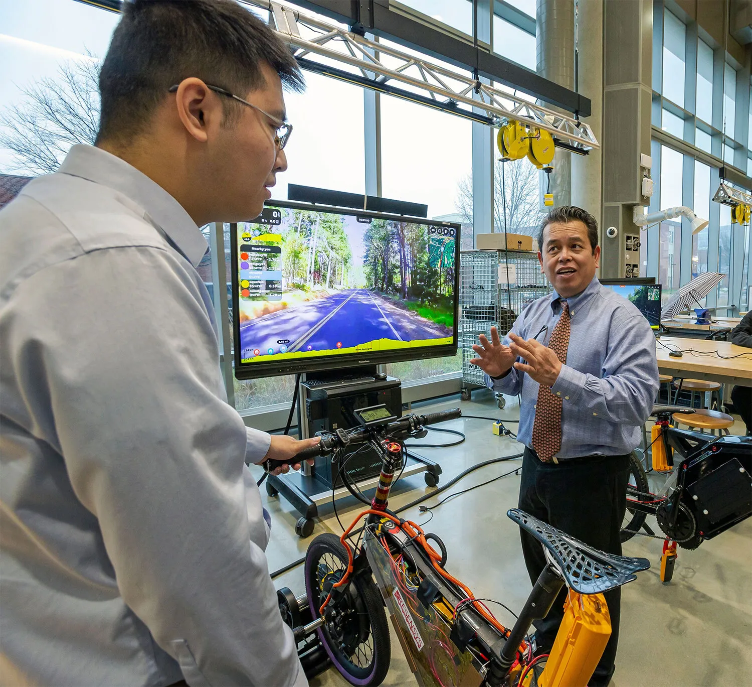 A professor talking to a student in a technical lab. They are discussing a simulation with an electric bike.