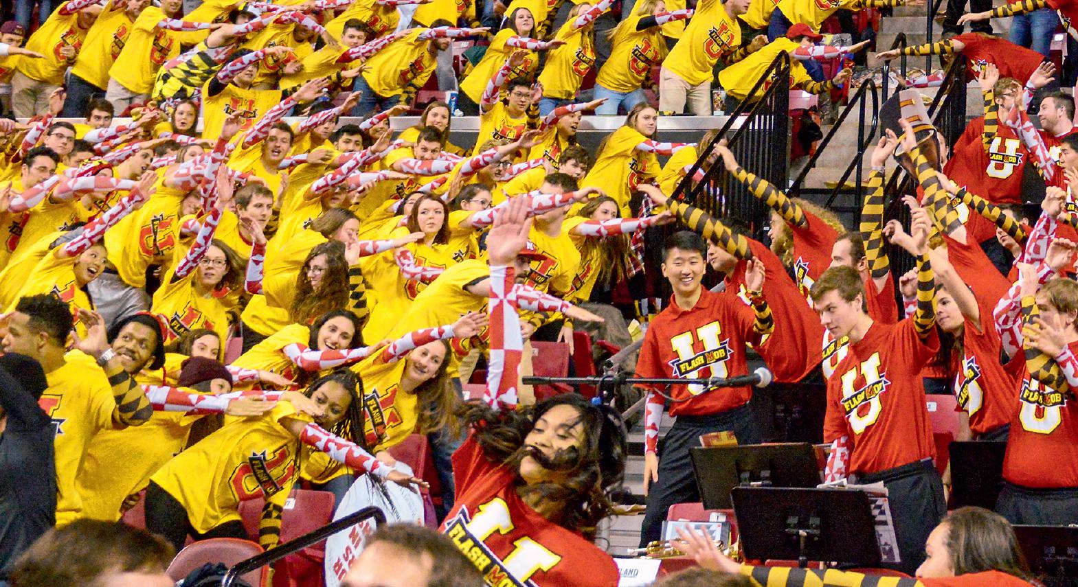 Lots of students dressed in yellow and red, swaying in a stadium