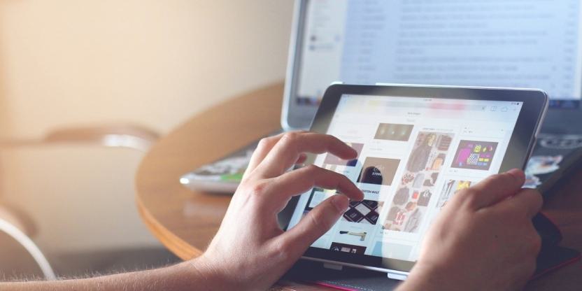 Close up view of hands holding a rectangular digital device while tapping an item on the screen.