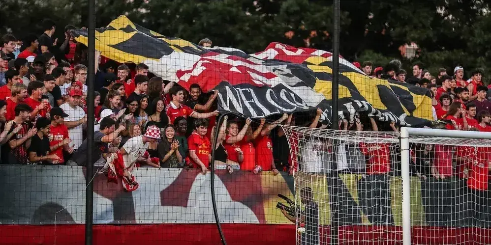 Fans hoisting Maryland flag in stands. Soccer net in front of stands