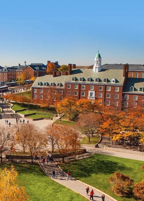 Red brick buildings on the UMD campus sit behind wide walkways cutting across green lawns and trees with yellow and orange leaves