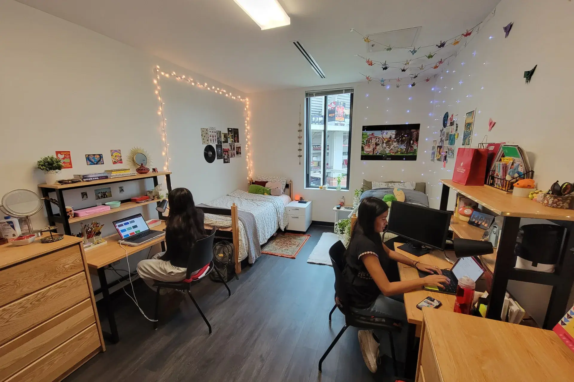 Dorm room with 2 girls working at laptops. Decorated with lights
