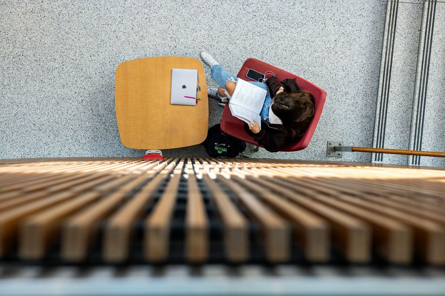 View from above, student looking at a notebook, laptop and pens, pencils on table